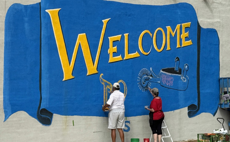 BIG WELCOME was painted on the wall of the Spur Ex-Student Association this summer by renowned artist Vicki Glass Diggs (here, with a little help on July 4 from Daniel Perez).